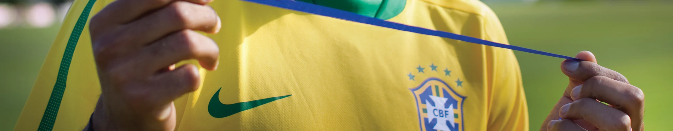 Mãos de um jogador da seleção seguram uma fita azul diante da camisa amarela.